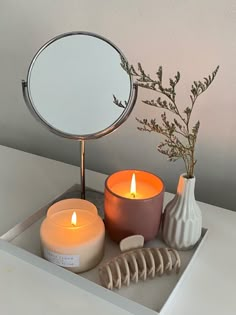 a mirror and some candles on a tray with a plant in the corner next to it