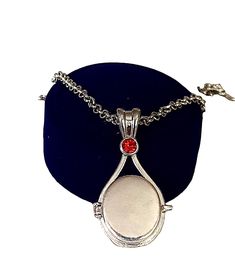 a necklace with a red stone in the center on a blue velvet cushioned surface