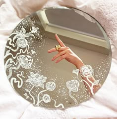 a person's hand pointing at the reflection in a round mirror on a bed