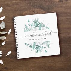 a wedding guest book on top of a wooden table next to some flowers and leaves