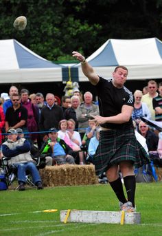 a man in a kilt throws a frisbee at an outdoor event while people watch