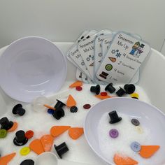 three white bowls filled with different colored buttons and plastic spoons on top of a table