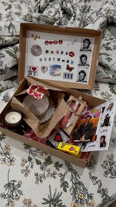 an open box on top of a bed filled with assorted items and papers next to a candle