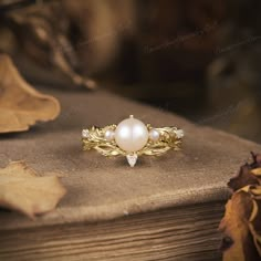 a pearl ring sitting on top of a wooden table next to leaves and a book