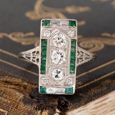 An Art Deco dinner ring studded with Old European cut diamonds, step cuts, and juicy green emeralds! This ring is full of impeccable detail, not to mention she covers up a significant amount of finger real estate! The color combination of diamonds and green emeralds is one that we cannot help but love, especially when set in an original Deco-era beauty. 18kt white gold Size 7.5 & fully resizable Diamond Measures: 5.67 x 5.67 x 3.94 mm Diamonds are estimated to be G/I colors & VVS/VS clarities. G Gia Certified Green Diamond Ring In Vintage Style, Green Diamond Ring With Single Cut Emerald Shape, Green Emerald Cut Diamond Ring With Single Cut Diamonds, Exquisite Green Emerald Platinum Ring, Art Deco Emerald And Diamond Ring For May Birthstone, Green Three Stone Platinum Ring, Art Deco Emerald Ring With Baguette Cut, Luxury Green Emerald Ring With Single Cut Diamonds, Platinum Emerald Ring With Diamond Accents