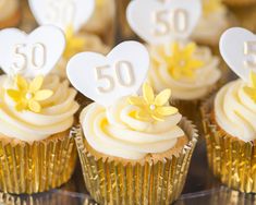 cupcakes with white frosting and gold foil wrappers are arranged in rows