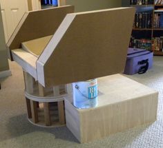 a cardboard house sitting on top of a table next to a book shelf and stairs