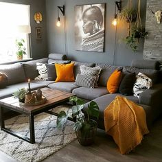 a living room with grey couches and orange pillows on the floor, plants in vases