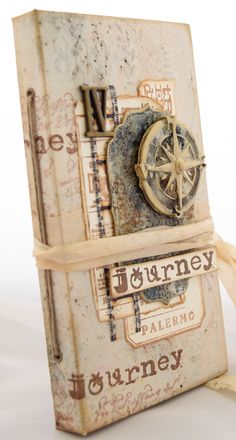 an old book with a compass on the cover and ribbon tied around it, sitting on a white surface