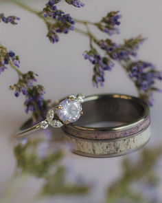 A matching purple wedding ring set from Staghead Designs sits on pastel purple paper surrounded by purple flowers. This ring set features our "Blossom" design engagement ring in 14K white gold with a round lavender quartz center stone and marquise and round floral diamond accents. Below sits our "Raptor" men's wedding band with a two channel design featuring antler and sugilite and fire and ice opal mixed inlays. Staghead Designs Engagement Rings, Antler Rings Women, Floral Wedding Ring Set, Purple Wedding Rings, Whiskey Barrel Wedding Ring, Antler Wedding Rings, Matching Wedding Ring Sets, Antler Wedding Band, Matching Ring Set