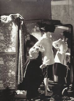 an old black and white photo of two women standing in front of a mirror with clothes hanging on it