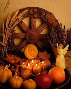 an arrangement of pumpkins, apples and candles in front of a wheel with angel figurines