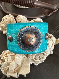 bracelet cuff, western jewelry  Genuine white distressed embossed leather strap has been given a turquoise dye and adorned with an antiqued copper flower concho.  The cuff is accented with four copper rivets and one copper snap has been placed to fit up to a 6 3/4" wrist. ✨I CAN ADD ANOTHER SNAP IF YOU WOULD LIKE A SMALLER OR LARGER SIZE BUT YOU NEED TO MESSAGE ME BEFORE PURCHASING  The last photo features other items available for purchase in my shop and not included in this listing As with all patina surfaces, color could transfer so extra care should be taken to avoid dye transfer- it is not water proof  other cuffs available https://www.etsy.com/shop/AsYouWishgallery?ref=seller-platform-mcnav§ion_id=18358191 I can also design this using vegan leather. If interested, just convo me and I Bohemian Festival Bracelet With Patina, Adjustable Western Cuff Bracelet For Festivals, Adjustable Western Style Cuff Bracelet For Festivals, Handmade Western Style Cuff Bracelets, Western Style Adjustable Cuff Bracelet For Festivals, Adjustable Western Style Festival Cuff Bracelet, Southwestern Style Turquoise Leather Bracelet For Festivals, Handmade Southwestern Turquoise Leather Bracelet, Southwestern Concho Cuff Bracelet For Festivals