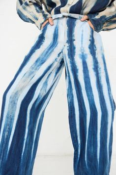 a woman standing in front of a white wall wearing blue and black tie dye pants