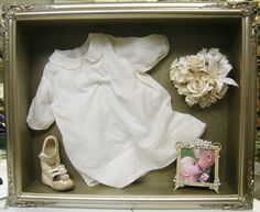 a baby's dress and shoes in a shadow box with flowers on the floor