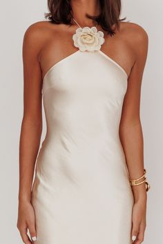 a woman wearing a white dress with a flower on the neck and gold bracelets