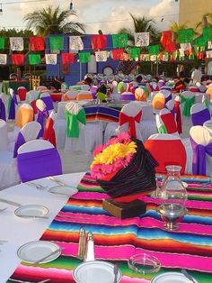 an outdoor event with tables and chairs covered in colorful cloths, decorated with flowers