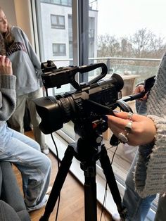 a woman standing next to a camera on top of a tripod in front of a window