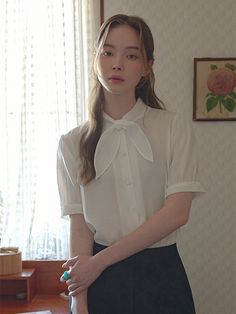 a woman standing in front of a window with a white shirt and black skirt on