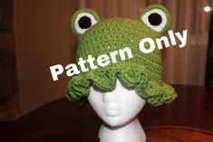 a crocheted frog hat with big eyes on top of a mannequin head