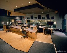 an empty room with multiple desks and monitors on the wall, in front of a large screen