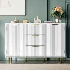 a white sideboard with gold handles and drawers in front of a green wall next to a plant