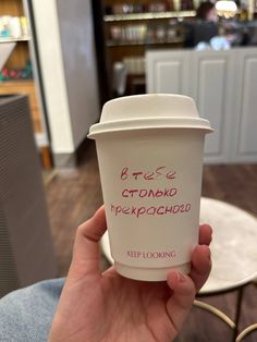 a person holding up a coffee cup with writing on the top and bottom in their left hand