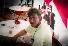 a man sitting at an outdoor table smiling for the camera