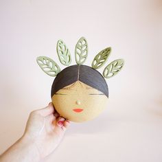 a person holding up a paper doll with leaves on it's head