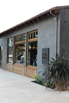 the outside of a restaurant with large windows and plants in pots on the side of the building