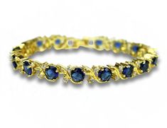 Indulge in the timeless elegance of this stunning Round Cut Swirl Blue Sapphire Bracelet, beautifully presented in a luxurious gift box. This exquisite bracelet features radiant blue sapphires, each meticulously round-cut and set in an elegant swirl design that adds a touch of sophistication to any outfit. Care Instructions: To maintain its brilliance, avoid exposure to harsh chemicals. Clean gently with a soft cloth and store in the provided gift box when not in use. Why You'll Love It: The vib Elegant Blue Bracelets For Formal Occasions, Classic Blue Bracelets For Wedding, Elegant Blue Bracelets For Anniversary, Elegant Blue Party Bracelets, Elegant Formal Blue Bracelets, Elegant Blue Jewelry With Jubilee Bracelet, Exquisite Blue Bracelets For Wedding, Elegant Cubic Zirconia Bracelet For Her, Elegant Sapphire Jewelry For Her