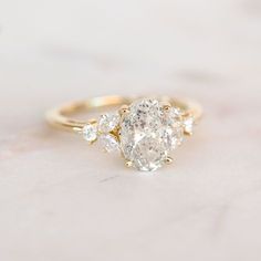 an oval diamond ring with three pear shaped diamonds on the band, set in yellow gold