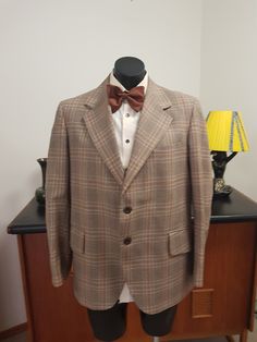 This jacket is from the 1970s in a pure wool and retailed by Fultons Mens wear store. The weight is all season in a light weight fabric from the English west country. Large lapels and flap pockets and two button closure  The condition is very good with no faults found EXCEPT that there is under arm staining in lining . Drycleaning should remove it And a dark mark on the sleeve  as in photo. Measurements are  Shoulder to shoulder 47cm Chest 116cm  Length shoulder to hem 74cm  Sleeves shoulder to Plaid Suits With Pockets For Fall, Fall Plaid Suits With Pockets, Brown Fall Suits With Lapel Collar, Brown Wool Sport Coat With Flat Front, Brown Flat Front Suits For Fall, Brown Flat Front Suit For Fall, Vintage Brown Tweed Jacket With Lapel Collar, Brown Wool Sport Coat With Suit Collar, Tailored Brown Outerwear In Formal Style