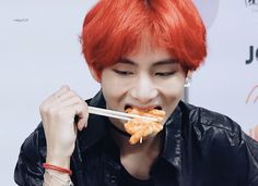 a man with red hair eating food from chopsticks