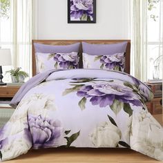 a bed with purple and white flowers on the comforter, pillows and pillow cases