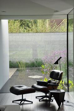 an eames chair and ottoman in front of a glass wall with flowers on it