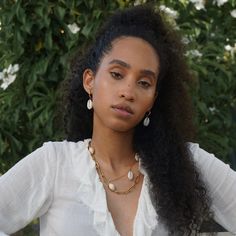 a close up of a person wearing a white shirt and necklace with flowers in the background