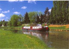 a red and white boat traveling down a river next to lush green grass on a sunny day