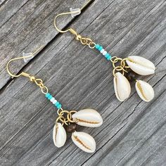 a pair of seashells with turquoise beads are hanging on a wooden plank surface