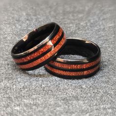 two rings with wood inlays sitting on top of a gray cloth covered surface