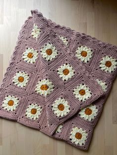 a crocheted blanket with white and yellow flowers on it sitting on top of a wooden floor