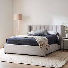 a bedroom with a bed, night stand and rugs on the hardwood flooring