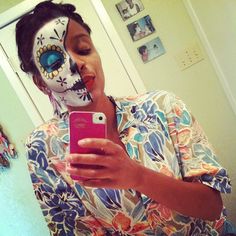 a woman with her face painted like a skeleton holding a cell phone in front of her face