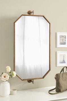 a mirror sitting on top of a white counter next to a purse and vase with flowers