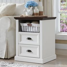 a living room with a white couch and two drawers on the end table in front of a window