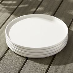 stack of white plates sitting on top of a wooden table next to a person's shadow