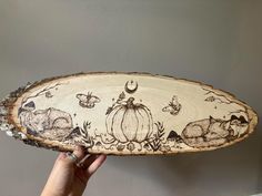 a person holding up a wooden plate with animals and pumpkins painted on the side