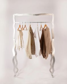 three sweaters hanging on a rack in front of a white wall with an iron frame