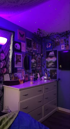 a bedroom with purple lighting and pictures on the wall above the dresser, along with other decorations