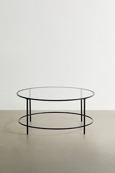 an oval glass coffee table with black metal frame on the bottom, against a white wall